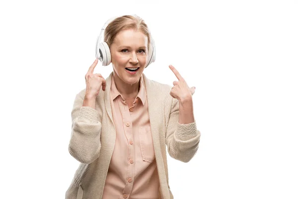 Smiling middle aged woman in headphones listening music and pointing with fingers Isolated On White — Stock Photo