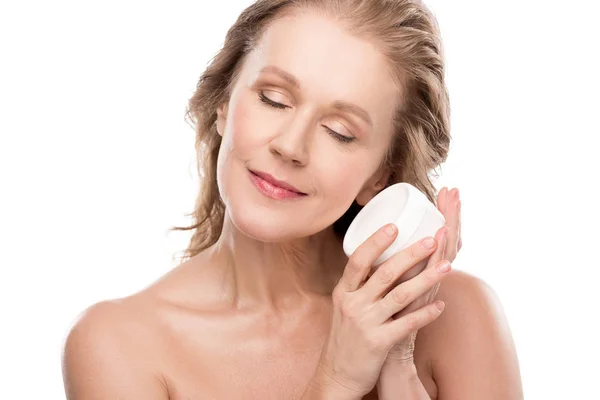 Привлекательная зрелая женщина держит контейнер с косметическим кремом изолированный на белом — стоковое фото