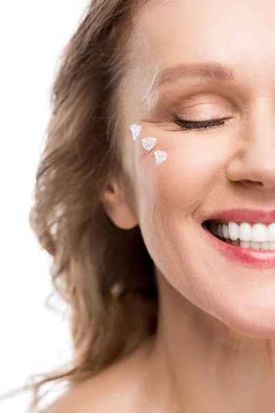 Sonriente mujer madura con crema cosmética en la cara aislado en blanco - foto de stock