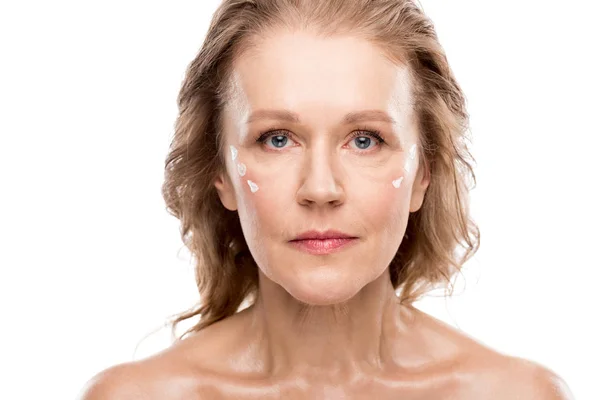 Зрелая женщина с косметическим кремом на лице, смотрящая в камеру Изолированный на белом — стоковое фото