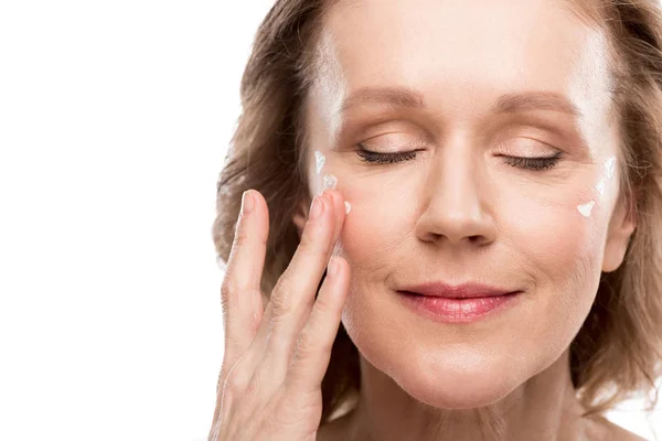 Reife Frau Anwendung kosmetischer Creme auf Gesicht isoliert auf weiß — Stockfoto