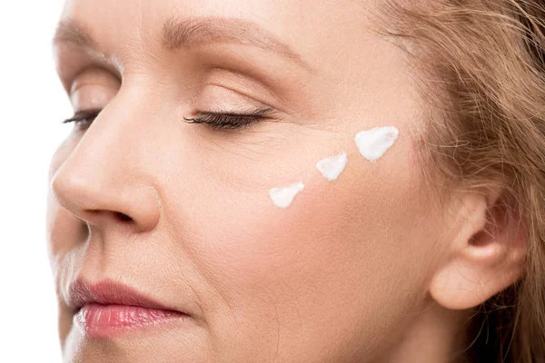 Gros plan de femme mature avec crème cosmétique sur le visage isolé sur blanc — Photo de stock