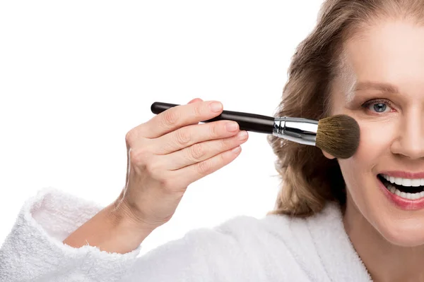 Vista cortada de mulher madura em roupão de banho usando escova de cosméticos ao aplicar maquiagem isolada em branco — Fotografia de Stock