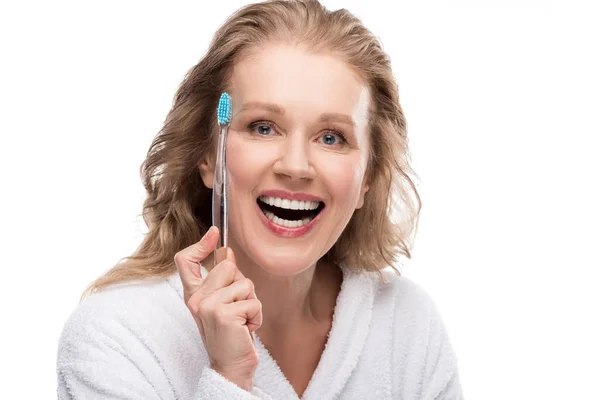 Femme d'âge moyen souriante en peignoir avec brosse à dents isolé sur blanc — Photo de stock