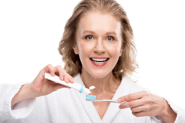 Усміхнена жінка середнього віку з зубною пастою та зубною щіткою ізольована на білому — стокове фото