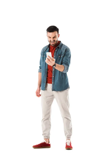 Irritated man in denim shirt using smartphone isolated on white — Stock Photo