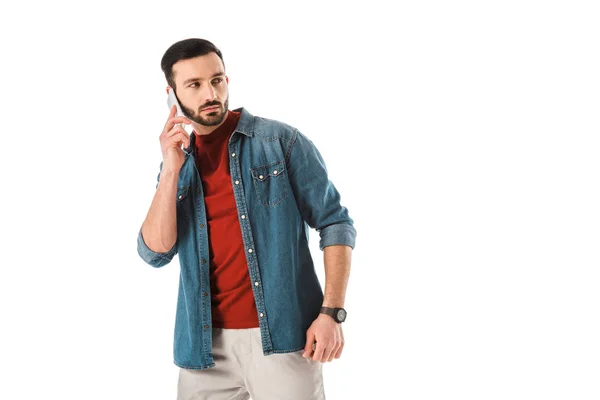 Homme barbu réfléchi en chemise denim regarder en arrière tout en utilisant smartphone isolé sur blanc — Photo de stock