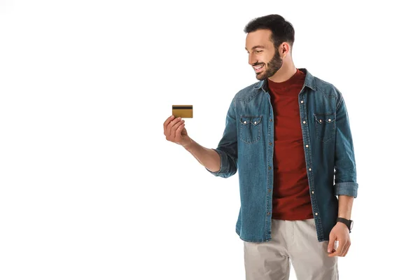 Homem bonito alegre na camisa do jeans que prende o cartão de crédito isolado no branco — Fotografia de Stock