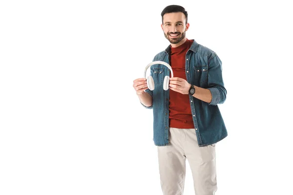 Fröhlicher Mann blickt in die Kamera, während er Kopfhörer isoliert auf weiß hält — Stockfoto
