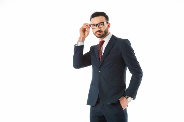 Uomo d'affari fiducioso toccando gli occhiali e guardando la fotocamera isolata su bianco — Foto stock