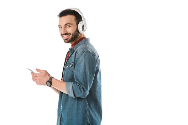 Hombre sonriente en auriculares con teléfono inteligente y mirando a la cámara aislada en blanco - foto de stock