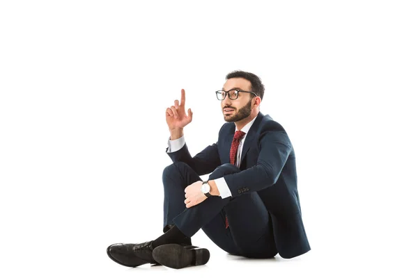 Sonriente hombre de negocios mostrando signo de idea mientras está sentado sobre fondo blanco - foto de stock