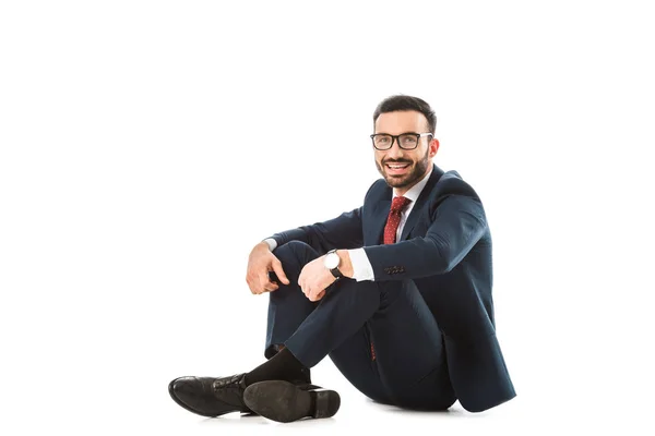 Homme d'affaires heureux dans des lunettes regardant la caméra tout en étant assis sur fond blanc — Photo de stock