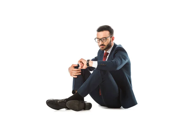 Homem de negócios pensativo olhando para assistir enquanto sentado no fundo branco — Fotografia de Stock