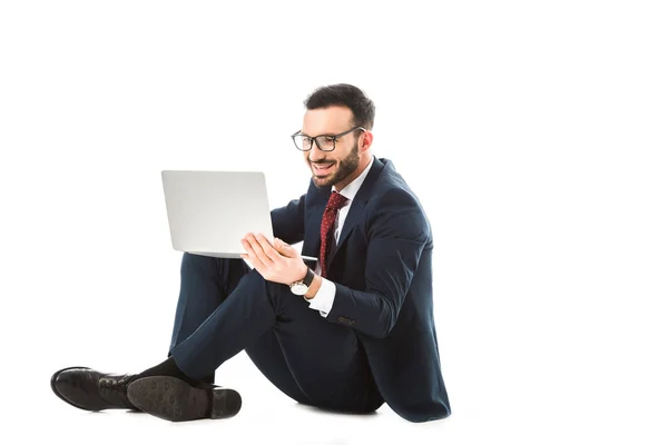 Uomo d'affari sorridente in occhiali utilizzando il computer portatile mentre seduto su sfondo bianco — Foto stock