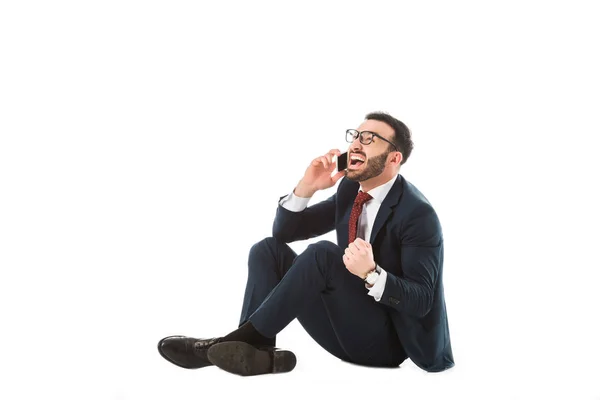 Hombre de negocios enojado peleando mientras está sentado y hablando en el teléfono inteligente sobre fondo blanco - foto de stock