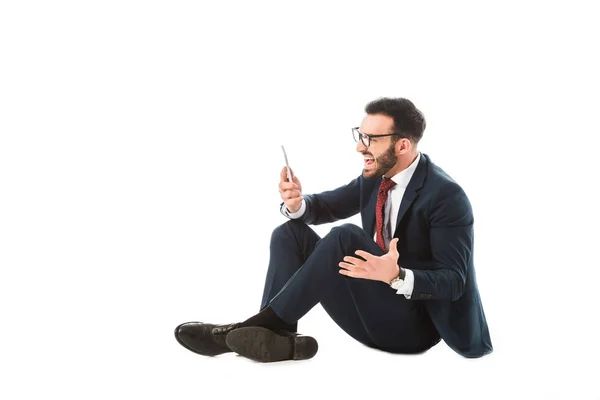 Irritated businessman screaming while sitting and using smartphone on white background — Stock Photo