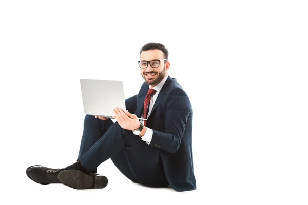 Lächelnder Geschäftsmann, der im Sitzen in die Kamera schaut und Laptop auf weißem Hintergrund benutzt — Stockfoto