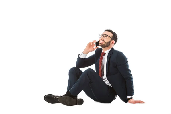 Fröhlicher Geschäftsmann schaut auf, während er sitzt und Smartphone auf weißem Hintergrund benutzt — Stockfoto