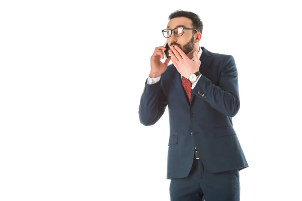 Sorprendido hombre de negocios que cubre la boca con la mano mientras habla en el teléfono inteligente aislado en blanco - foto de stock