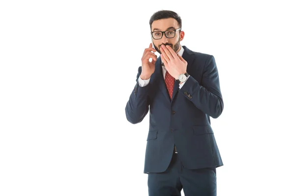 Здивований бізнесмен тримає руку на роті, розмовляючи на смартфоні ізольовано на білому — стокове фото