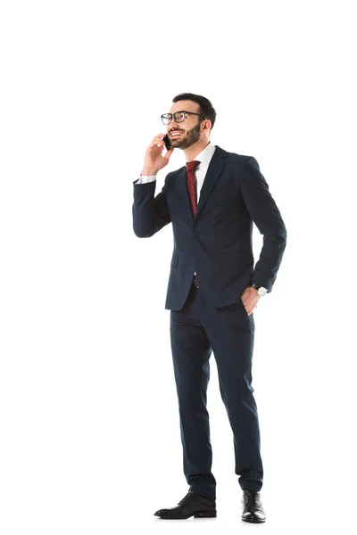 Alegre hombre de negocios de pie con la mano en el bolsillo y hablando en el teléfono inteligente aislado en blanco - foto de stock