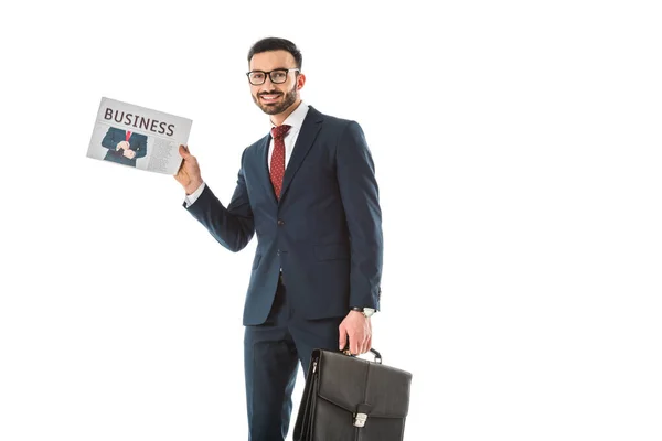Smiling handsome businessman with briefcase holding newspaper and looking at camera isolated on white — Stock Photo