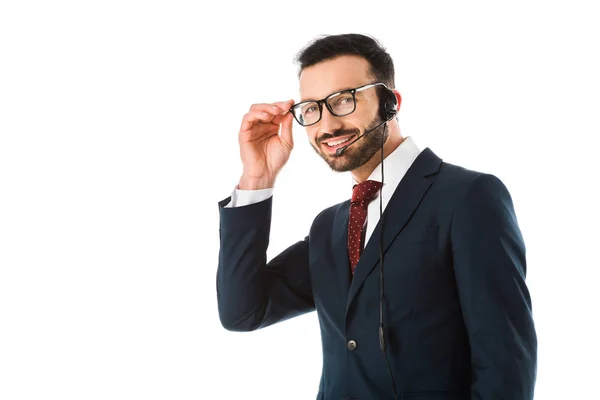 Sonriente operador del centro de llamadas en auriculares mirando a la cámara y tocando gafas aisladas en blanco - foto de stock