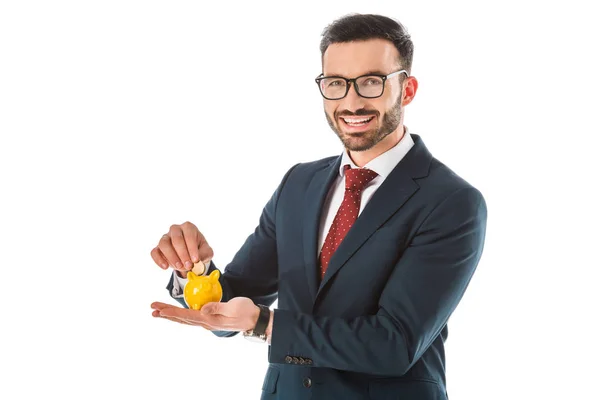 Alegre hombre de negocios poniendo moneda en alcancía y mirando a la cámara aislada en blanco - foto de stock