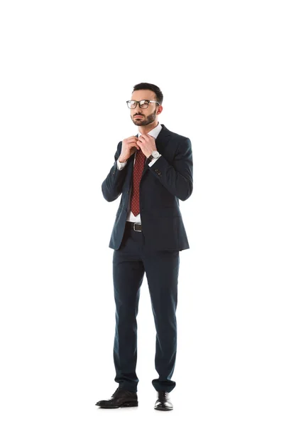 Serio uomo d'affari in abito nero toccare cravatta e guardando lontano isolato su bianco — Foto stock