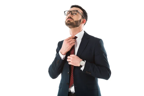 Guapo empresario confiado en traje negro y gafas tocando corbata aislada en blanco - foto de stock