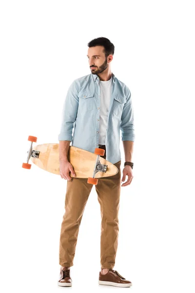Guapo barbudo hombre sosteniendo longboard y mirando hacia otro lado aislado en blanco - foto de stock