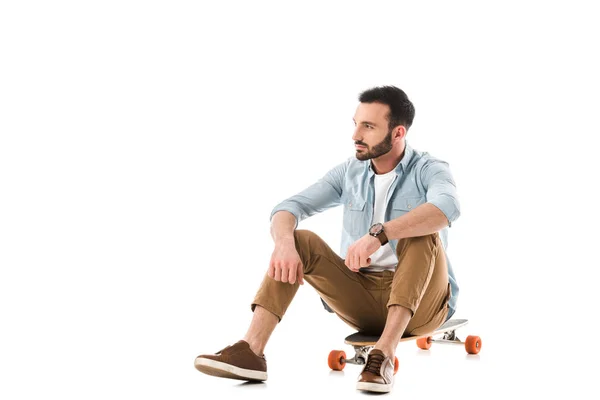 Nachdenklicher bärtiger Mann auf Longboard sitzend und isoliert auf weißem Grund wegschauend — Stockfoto