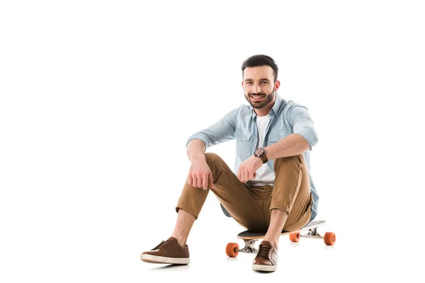 Fröhlicher Mann, der auf Longboard sitzt und isoliert auf weiß in die Kamera schaut — Stockfoto