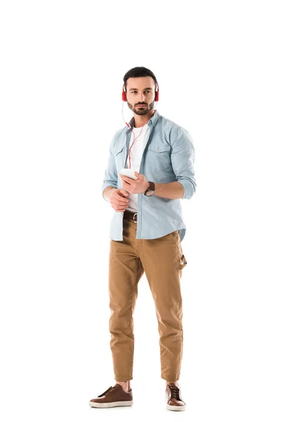 Hombre pensativo escuchar música en los auriculares y la celebración de teléfono inteligente aislado en blanco - foto de stock