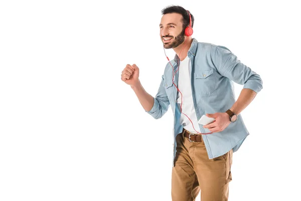 Cheerful man dancing while listening music in headphones and holding smartphone isolated on white — Stock Photo