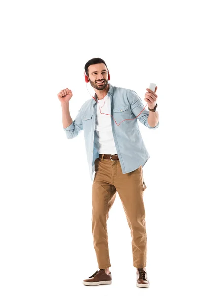 Hombre feliz en auriculares escuchando música y sosteniendo el teléfono inteligente mientras baila aislado en blanco - foto de stock