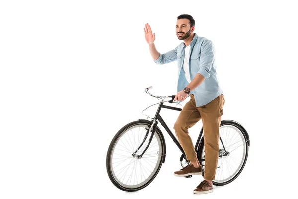 Homem alegre com bicicleta mostrando Olá gesto e olhando para longe isolado no branco — Fotografia de Stock