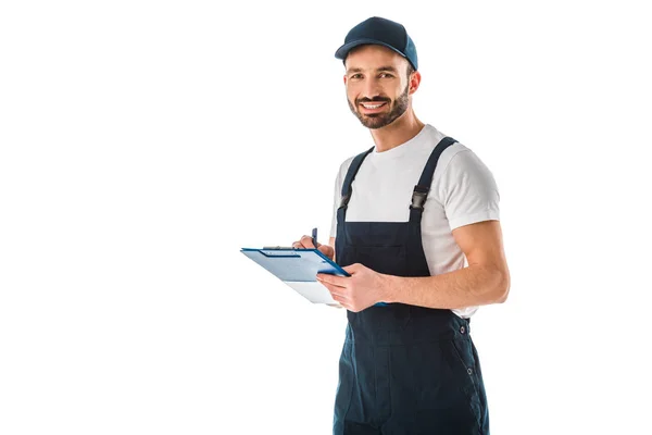 Lächelnder Zusteller, der auf Klemmbrett schreibt und isoliert auf weiß in die Kamera schaut — Stockfoto