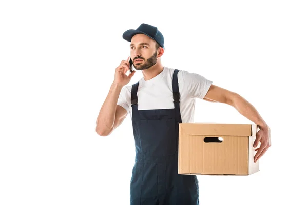 Homem de entrega atencioso falando no smartphone enquanto segurando caixa de papelão isolado no branco — Fotografia de Stock