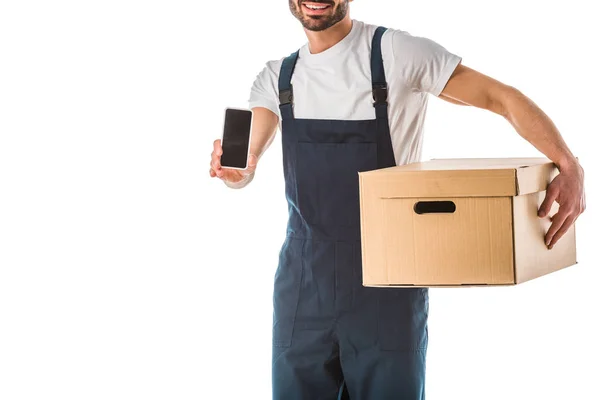Vista recortada del repartidor sonriente con caja de cartón que sostiene el teléfono inteligente con pantalla en blanco aislado en blanco - foto de stock