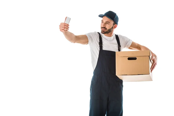 Schöner Zusteller macht Selfie mit Smartphone, während er Pappschachtel isoliert auf weiß hält — Stockfoto