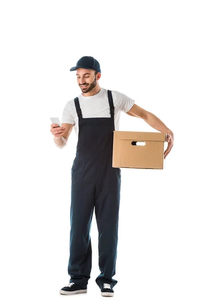 Усміхнений чоловік доставки використовує смартфон, тримаючи картонну коробку ізольовано на білому — стокове фото