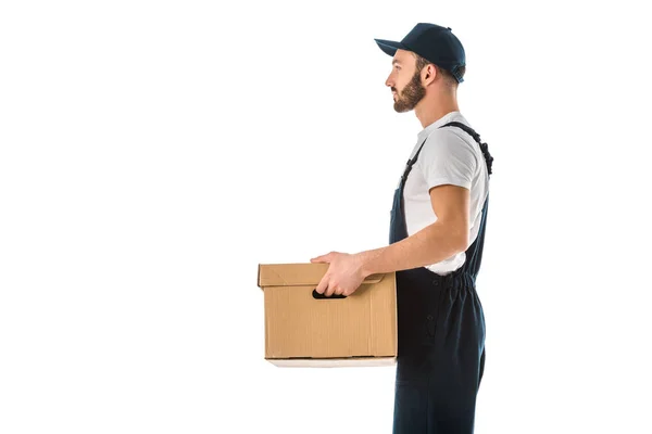 Side view of delivery man in overalls and cap holding cardboard box isolated on white — Stock Photo