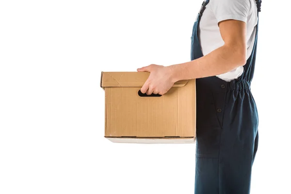 Обрізаний вид доставки людини в комбінезоні, що тримає картонну коробку ізольовано на білому — стокове фото