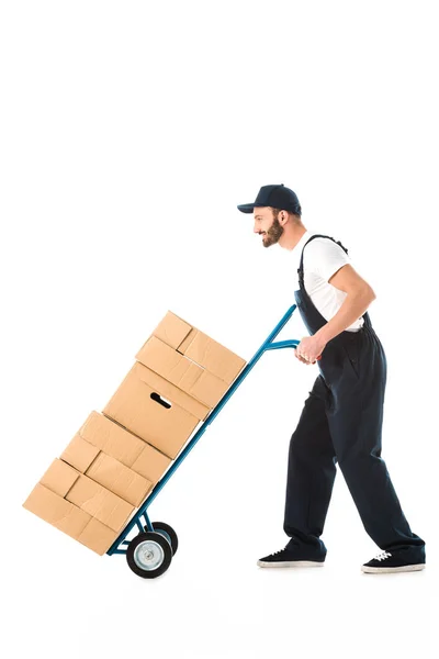 Vista lateral del repartidor hombre transportando cajas de cartón cargadas en camión de mano aislado en blanco - foto de stock