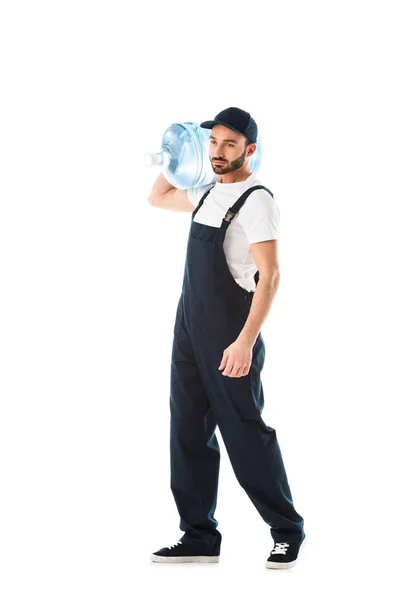 Serious delivery man in overalls carrying bottle of water isolated on white — Stock Photo