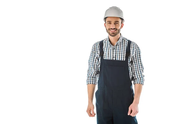 Trabajador de la construcción sonriente en overoles y casco mirando a la cámara aislada en blanco - foto de stock