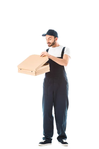 Усміхнений чоловік доставки в комбінезоні, дивлячись в коробку для піци ізольовано на білому — стокове фото