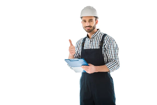 Улыбающийся строитель с планшетом, показывающий большой палец и смотрящий в камеру, изолированную на белом — стоковое фото